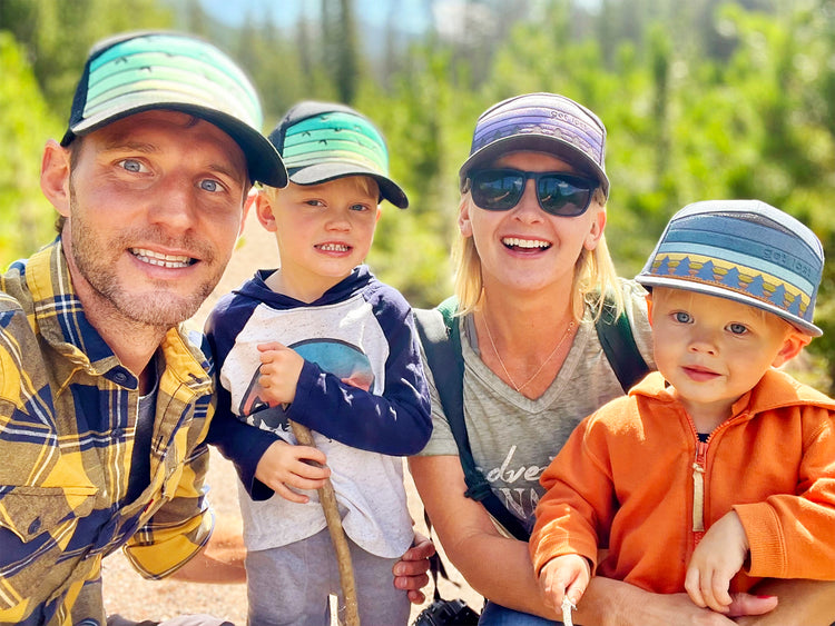 The Wild &amp; Free family, two parents and their two young sons, smiling in Wild &amp; Free hats on a forest trail