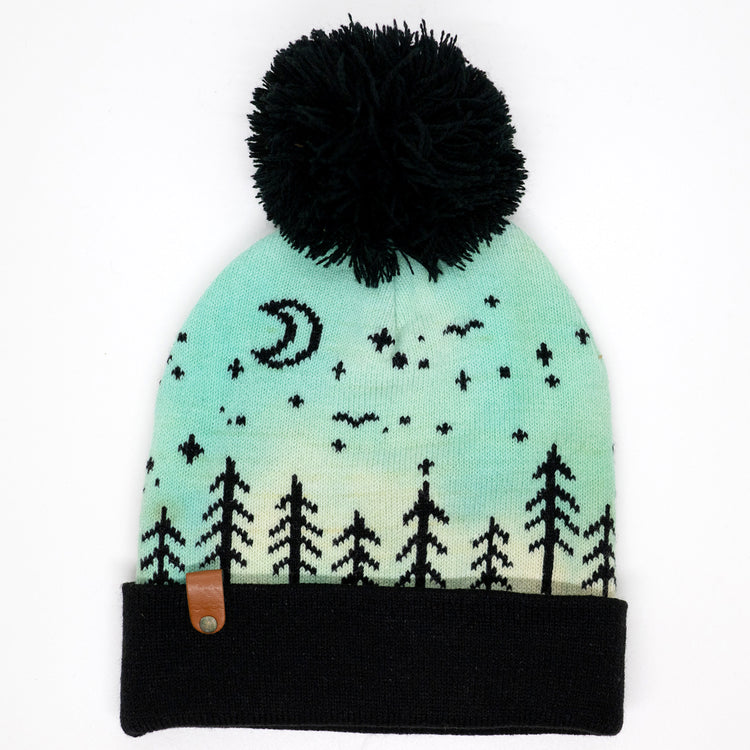 Hand-dyed kids winter beanie fading from yellow to light blue-green with black pom-pom and forest design.
