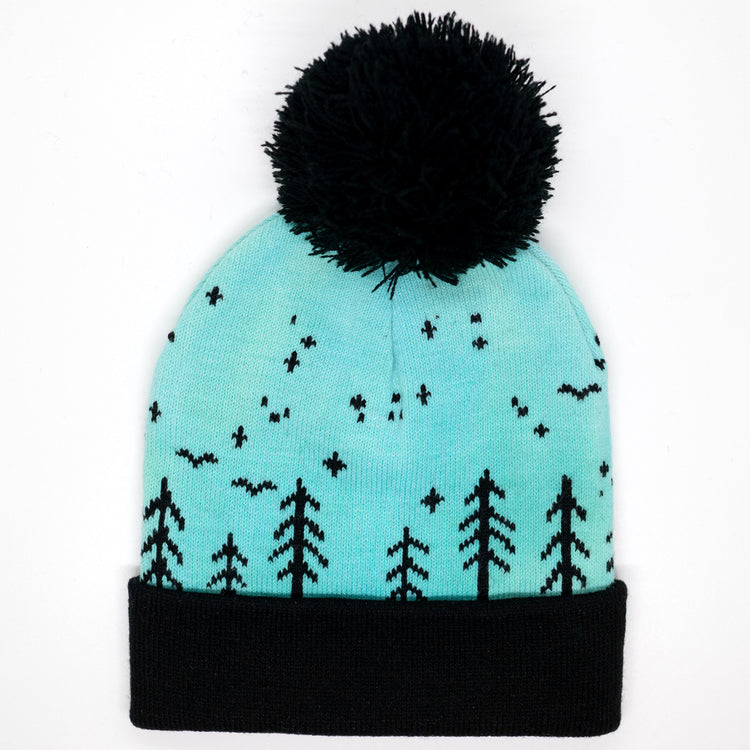 Hand-dyed kids winter beanie fading from blue to green with black pom-pom and forest design.