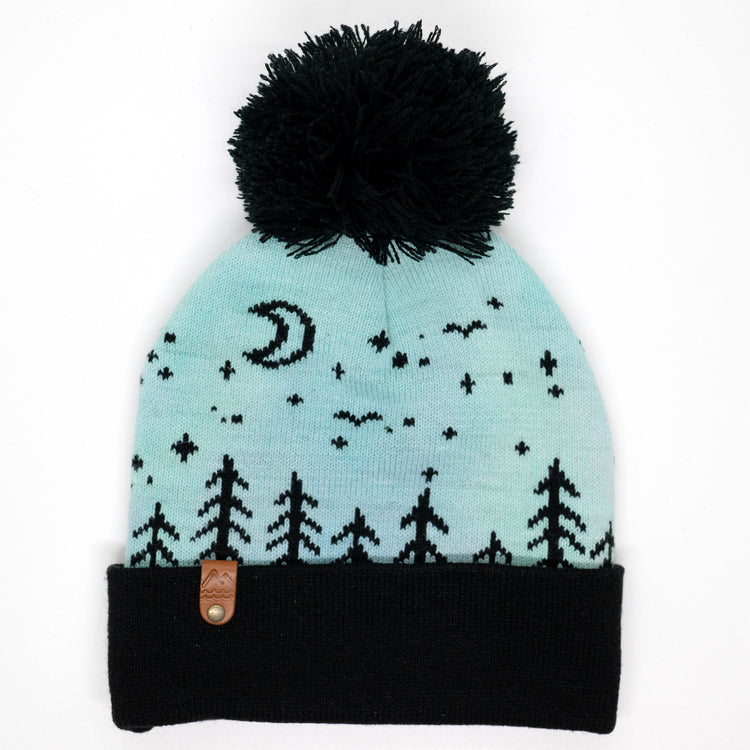 Hand-dyed kids winter beanie fading from blue to green and purple with black pom-pom and forest design.