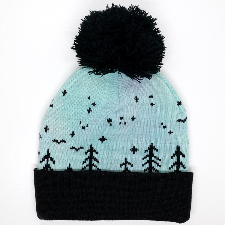 Hand-dyed kids winter beanie fading from blue to green and purple with black pom-pom and forest design.