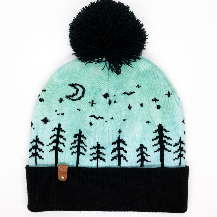 Hand-dyed kids winter beanie in blue and green with black pom-pom and forest design.