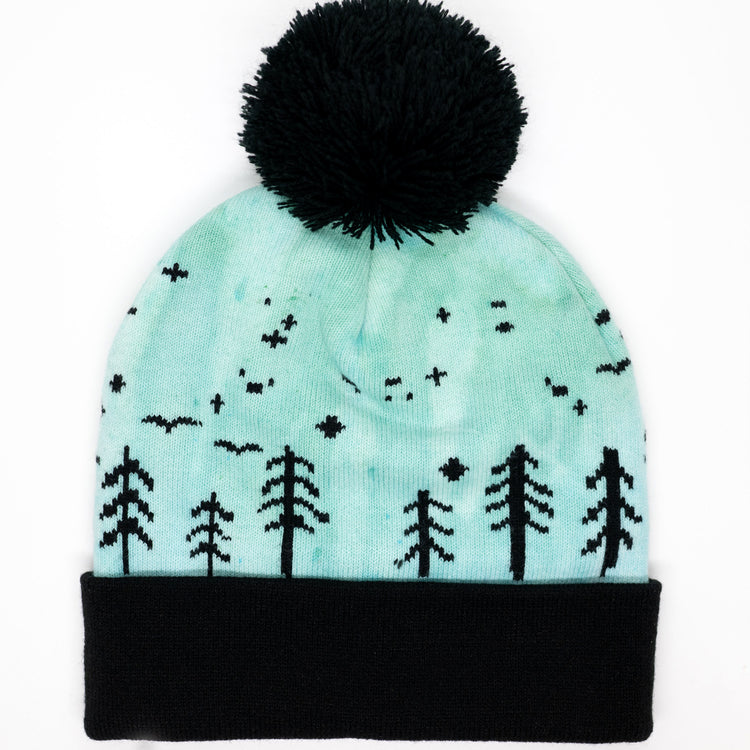 Hand-dyed kids winter beanie in blue and green with black pom-pom and forest design.